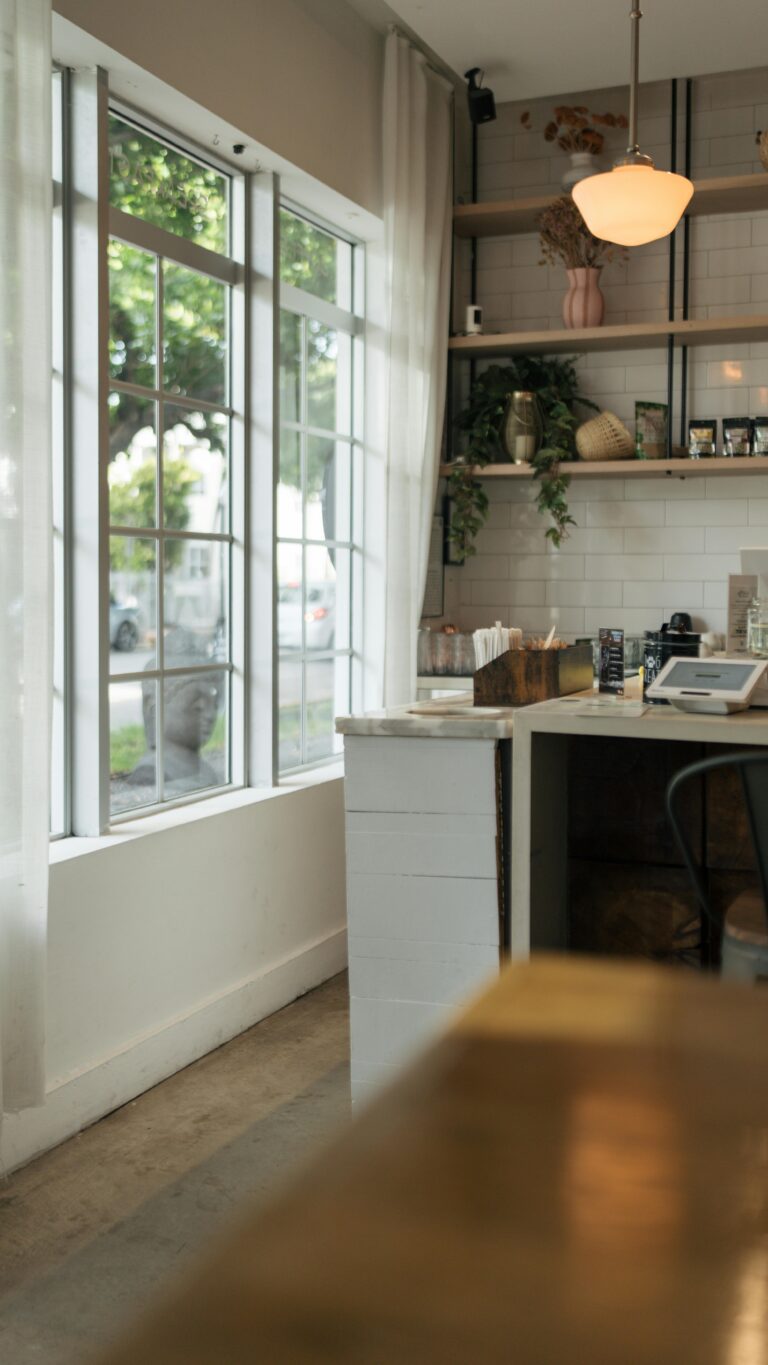 A well-lit modern coffee shop with natural light streaming through large windows and elegant decor.