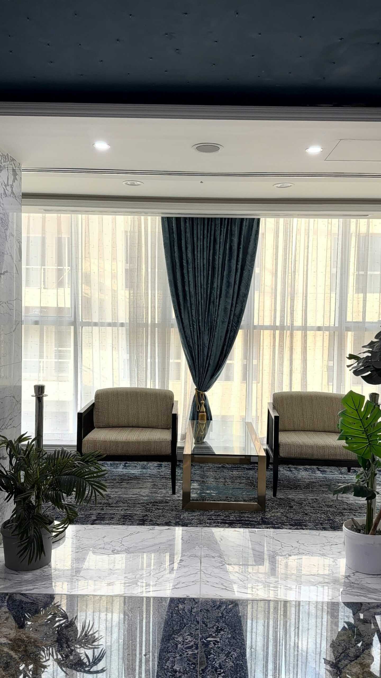 A stylish waiting area featuring modern furniture, blue drapes, and natural light.